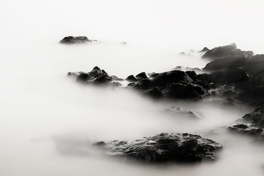 Black rocks in white sea fog, in black and white