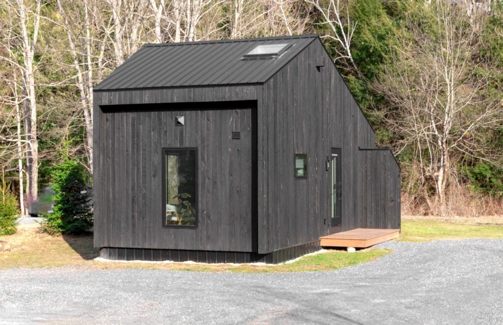 A small black timber house on gravel