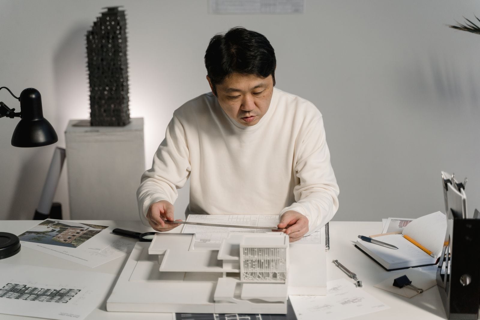 An architect checking a white card model at the studio desk