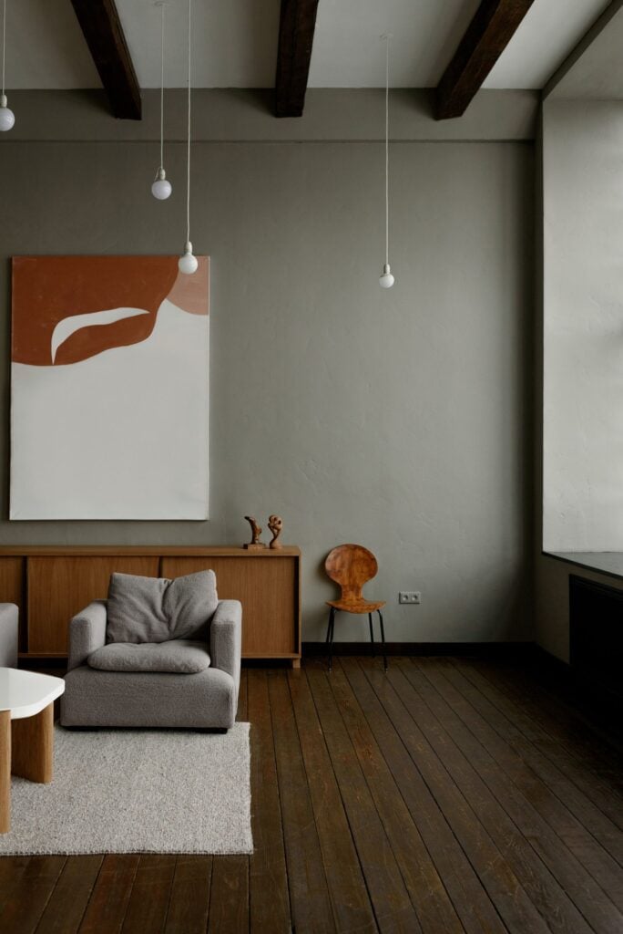 A grey room with an armchair, a sideboard and a large artwork