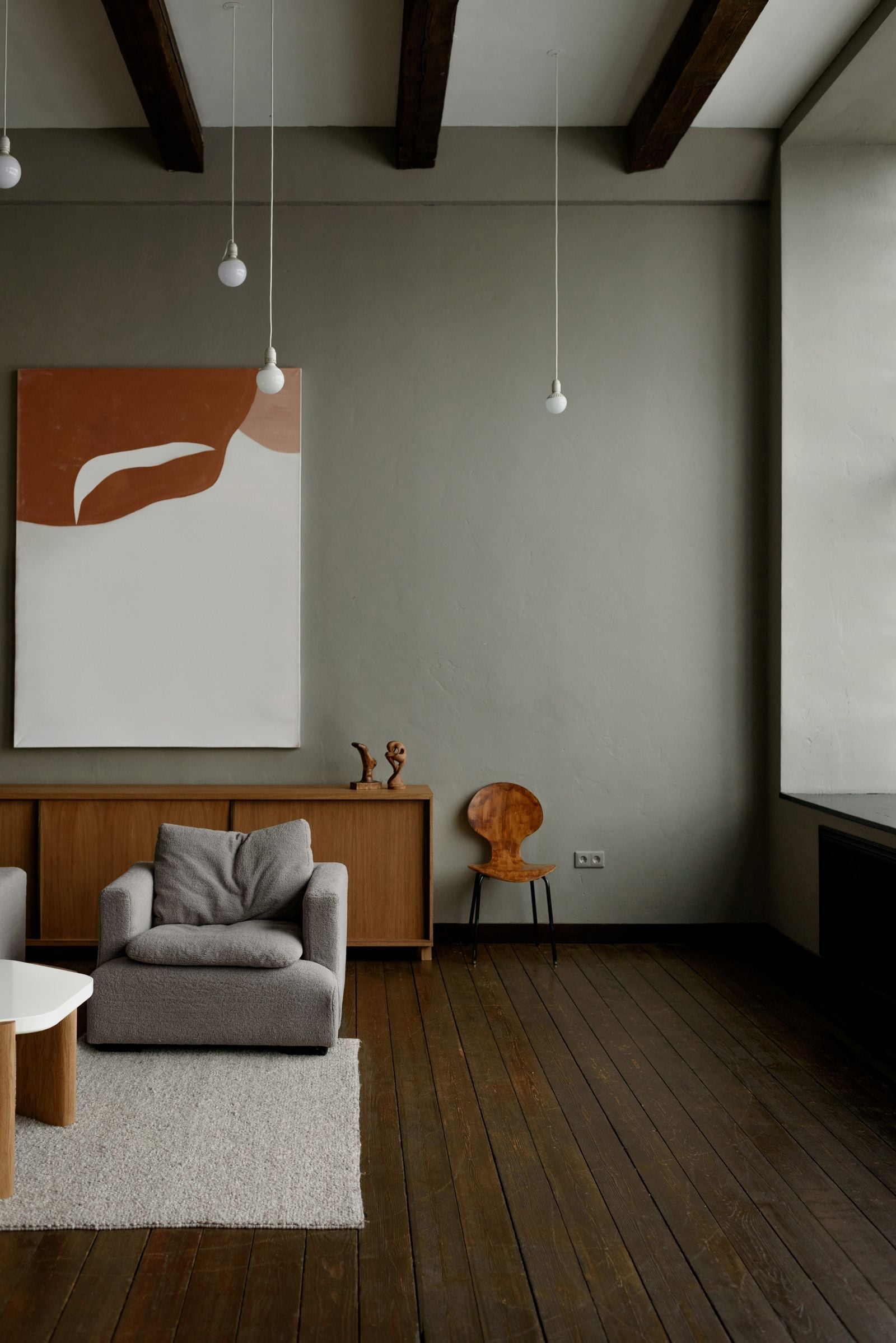 A grey room with an armchair, a sideboard and a large artwork