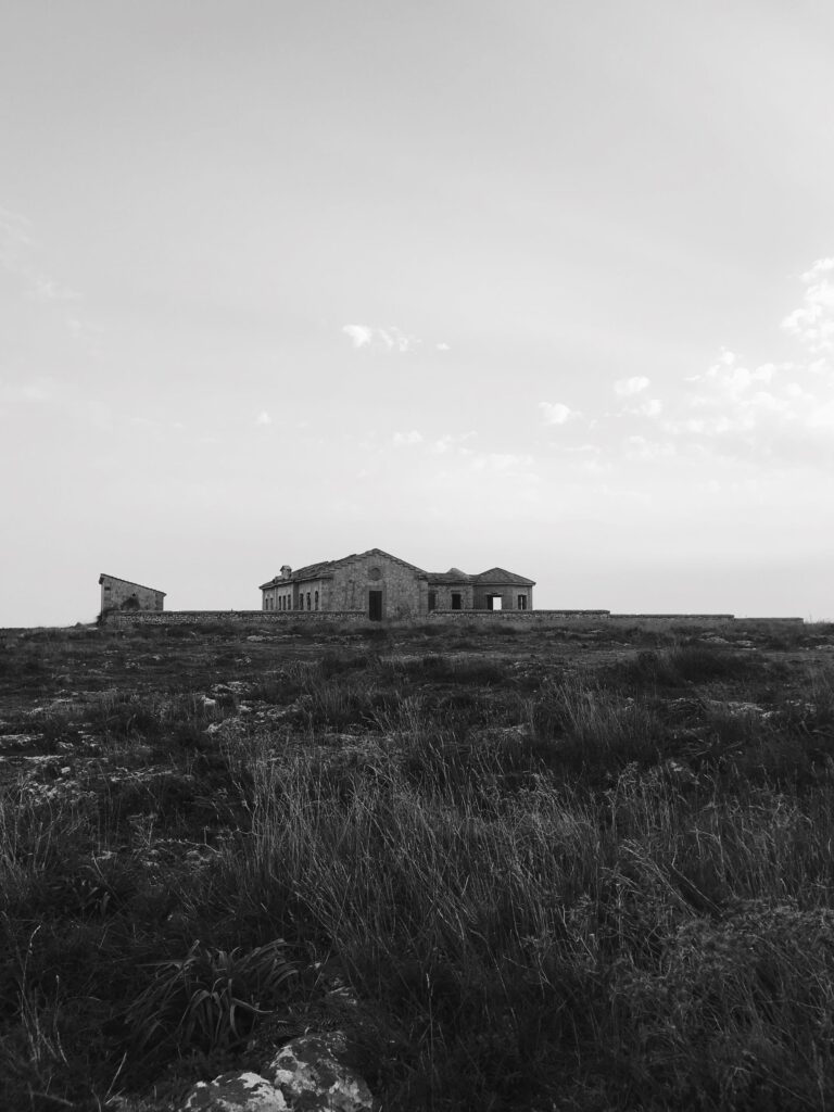 A distant house on open moorland under a big sky, in black and white