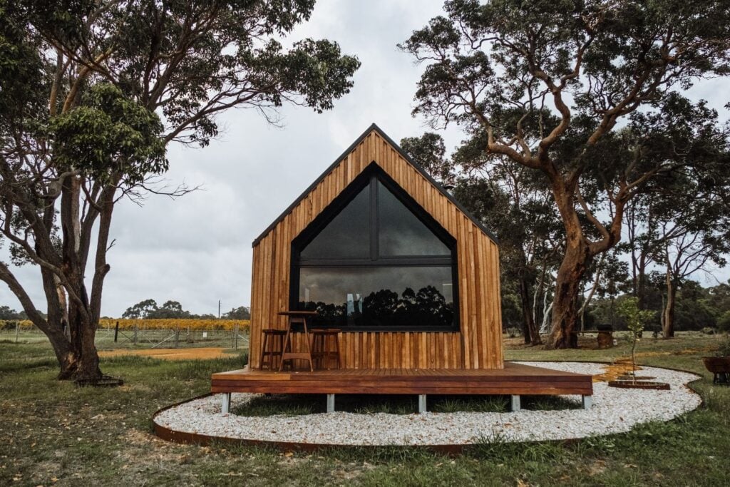 A warm timber gable house with a large window on a gravel plinth