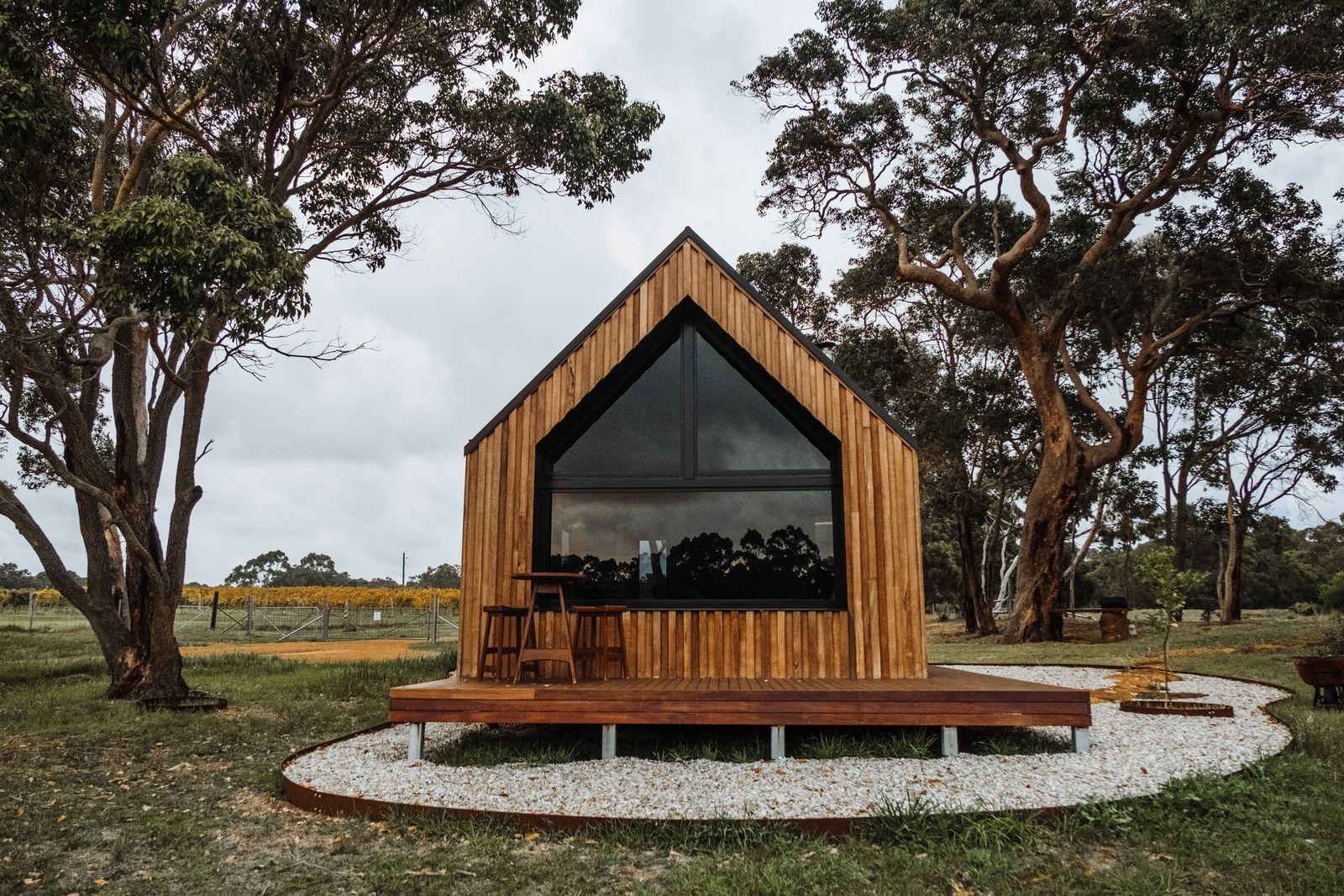 A warm timber gable house with a large window on a gravel plinth