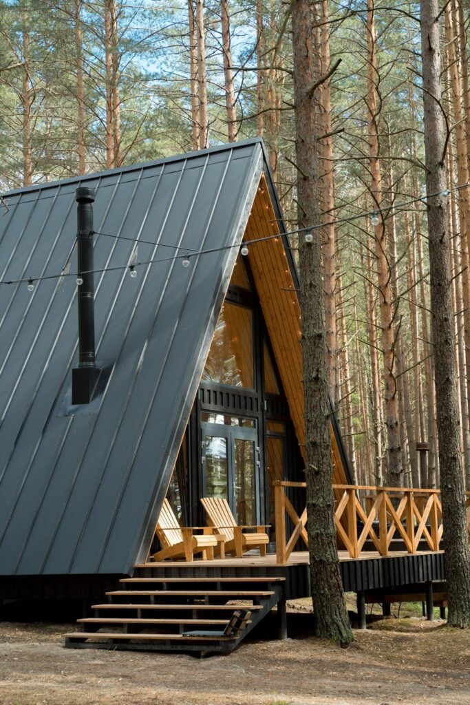 An A-frame cabin with a dark metal roof among tall pines