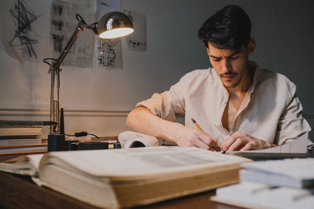 An architect drawing by hand under a desk lamp