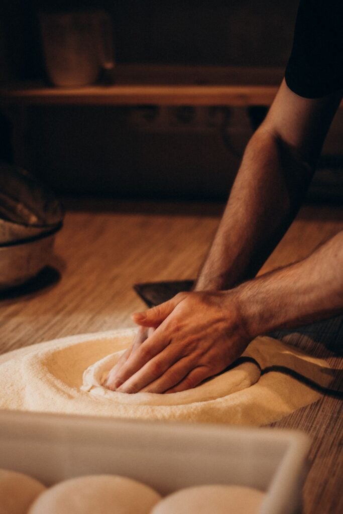 Hands pressing dough on a wooden bench in warm light