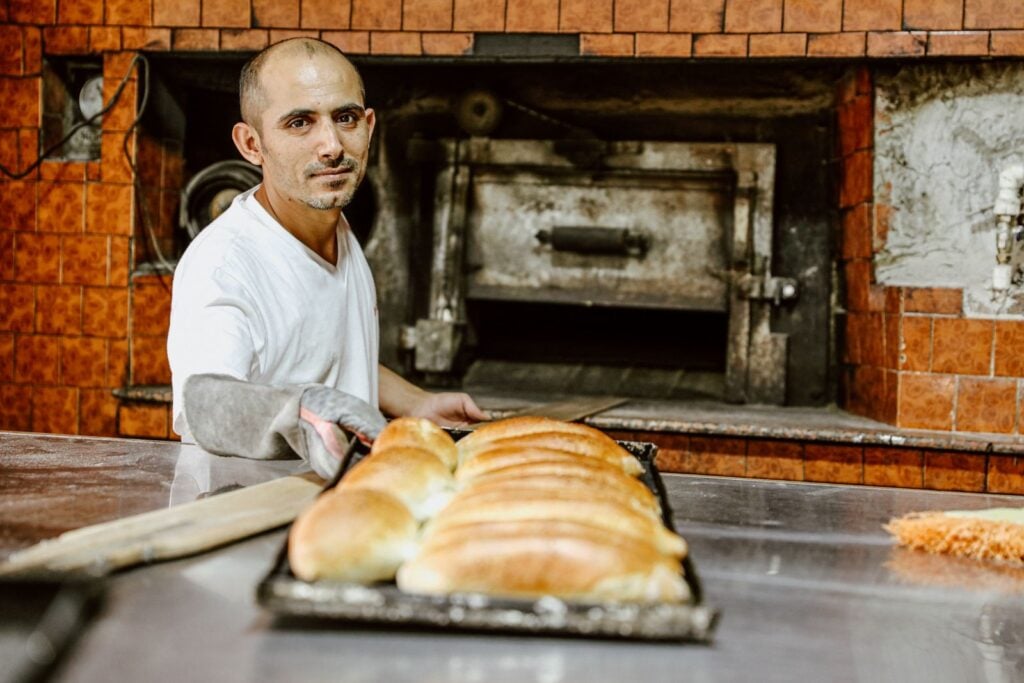 Smiling baker pulling a tray of bread from a tiled oven