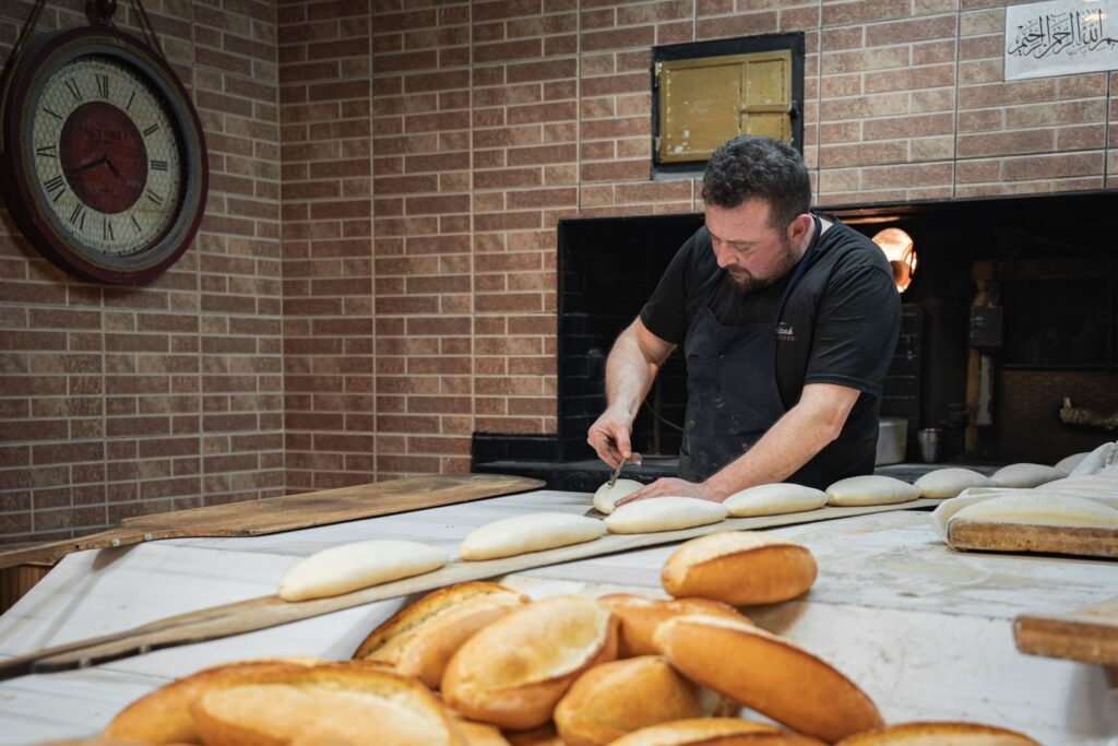 Baker shaping rolls in front of a brick wall