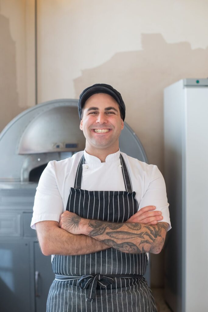 Tomás, baker, smiling with arms crossed in a striped apron