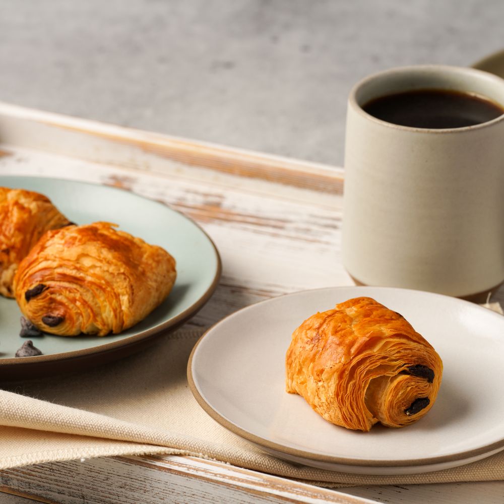 Pain au chocolat and a croissant on plates with a cup of coffee