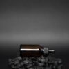 Amber dropper bottle of beard oil lying on black stones