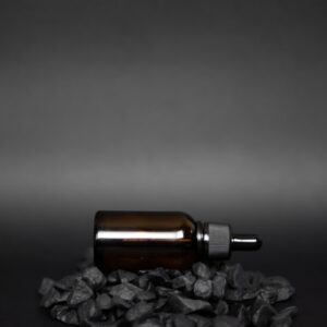 Amber dropper bottle of beard oil lying on black stones