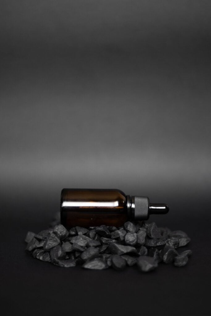 Amber dropper bottle of beard oil lying on black stones