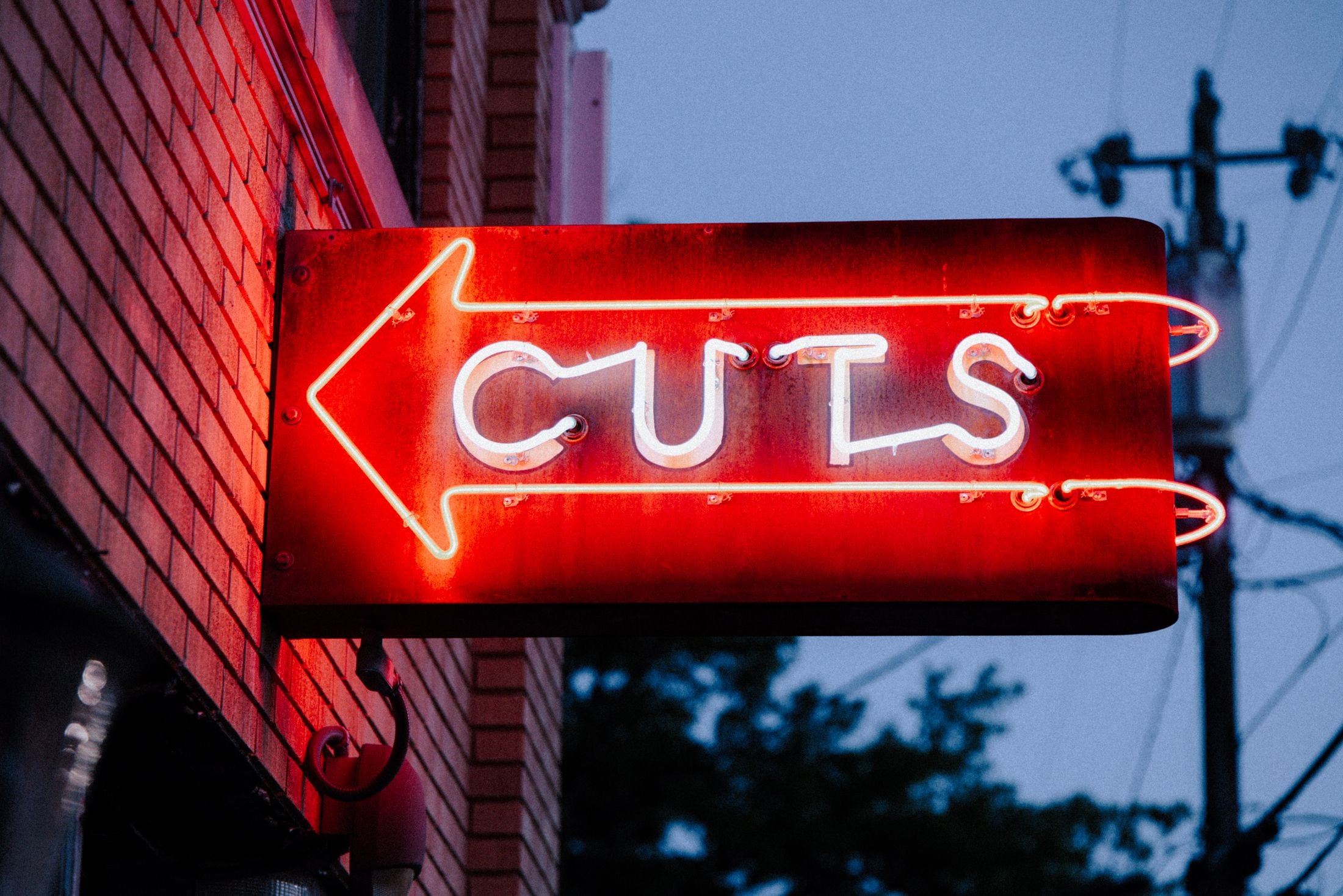 Red neon sign reading Cuts on a brick wall at dusk