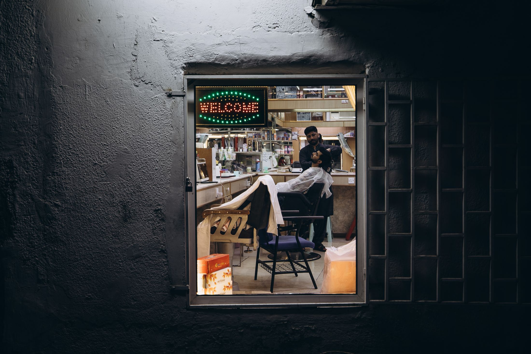 Lit barbershop window in a dark wall at night