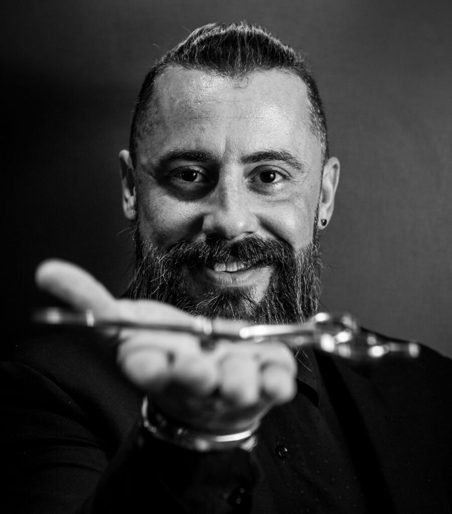 Smiling bearded barber holding out a pair of scissors, black and white