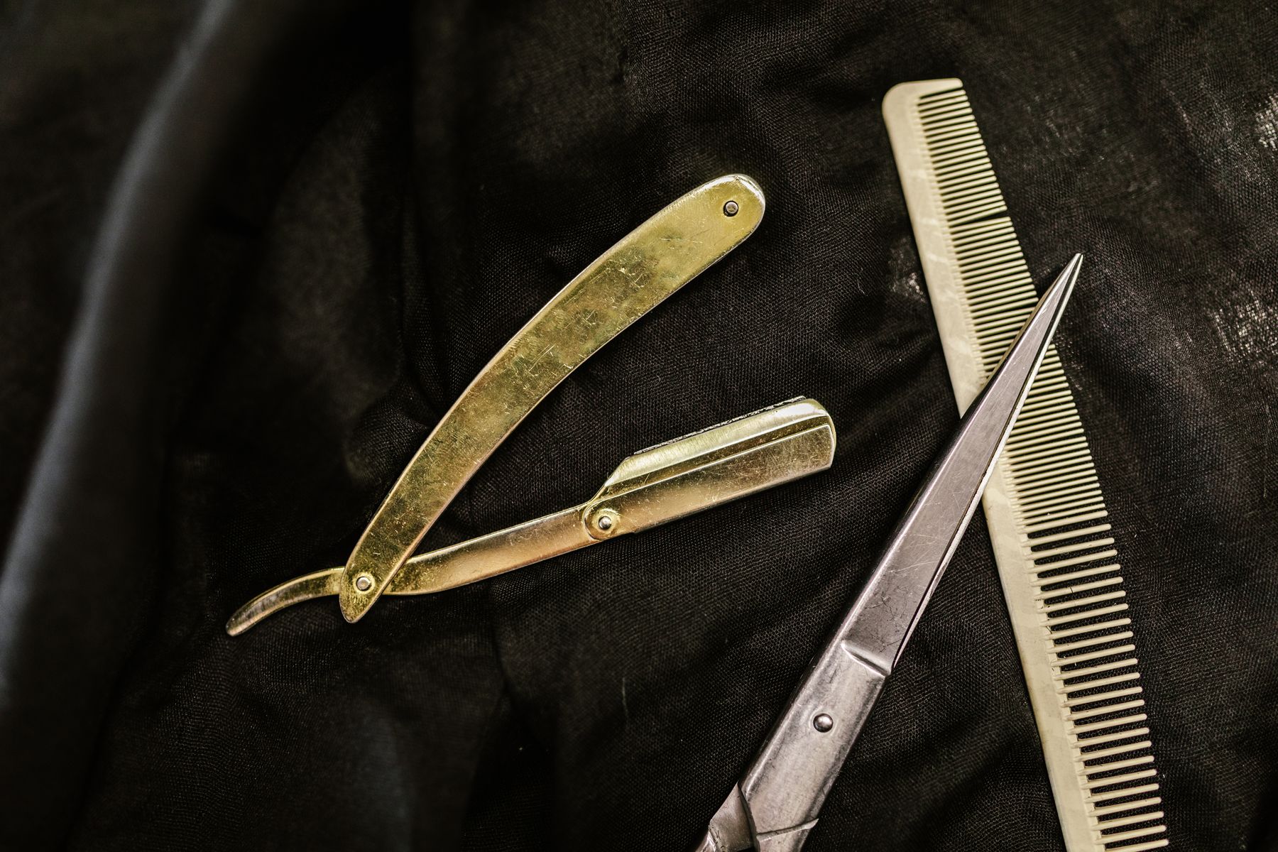 Brass straight razor, scissors and comb on black leather