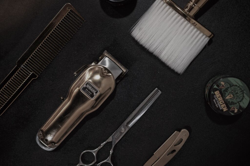 Clipper, scissors, comb and neck brush on a black surface