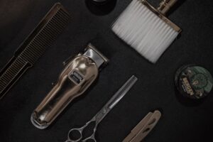 Clipper, scissors, comb and neck brush on a black surface