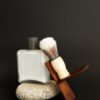 White aftershave bottle with a shaving brush on a stone, dark backdrop