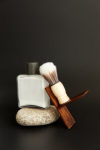 White aftershave bottle with a shaving brush on a stone, dark backdrop