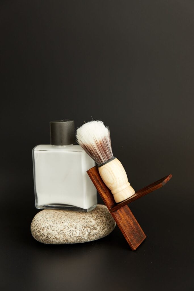 White aftershave bottle with a shaving brush on a stone, dark backdrop