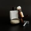 Safety razor, shaving brush on a walnut stand and aftershave on a dark backdrop