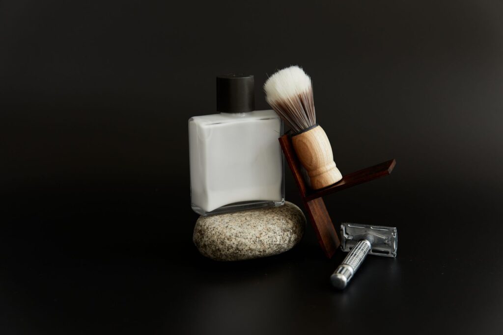 Safety razor, shaving brush on a walnut stand and aftershave on a dark backdrop