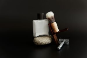 Safety razor, shaving brush on a walnut stand and aftershave on a dark backdrop
