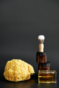 Natural sponge, amber jars, tonic and a shaving brush on a dark backdrop