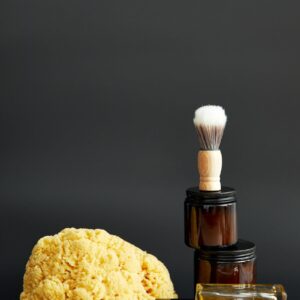 Natural sponge, amber jars, tonic and a shaving brush on a dark backdrop