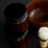 Dark jar of beard balm beside a wooden bowl and brush