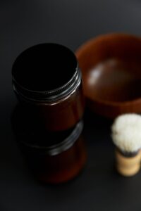 Dark jar of beard balm beside a wooden bowl and brush
