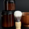Two amber jars of shave cream with a shaving brush and wooden bowl