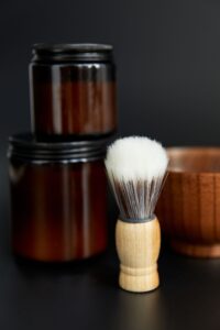 Two amber jars of shave cream with a shaving brush and wooden bowl