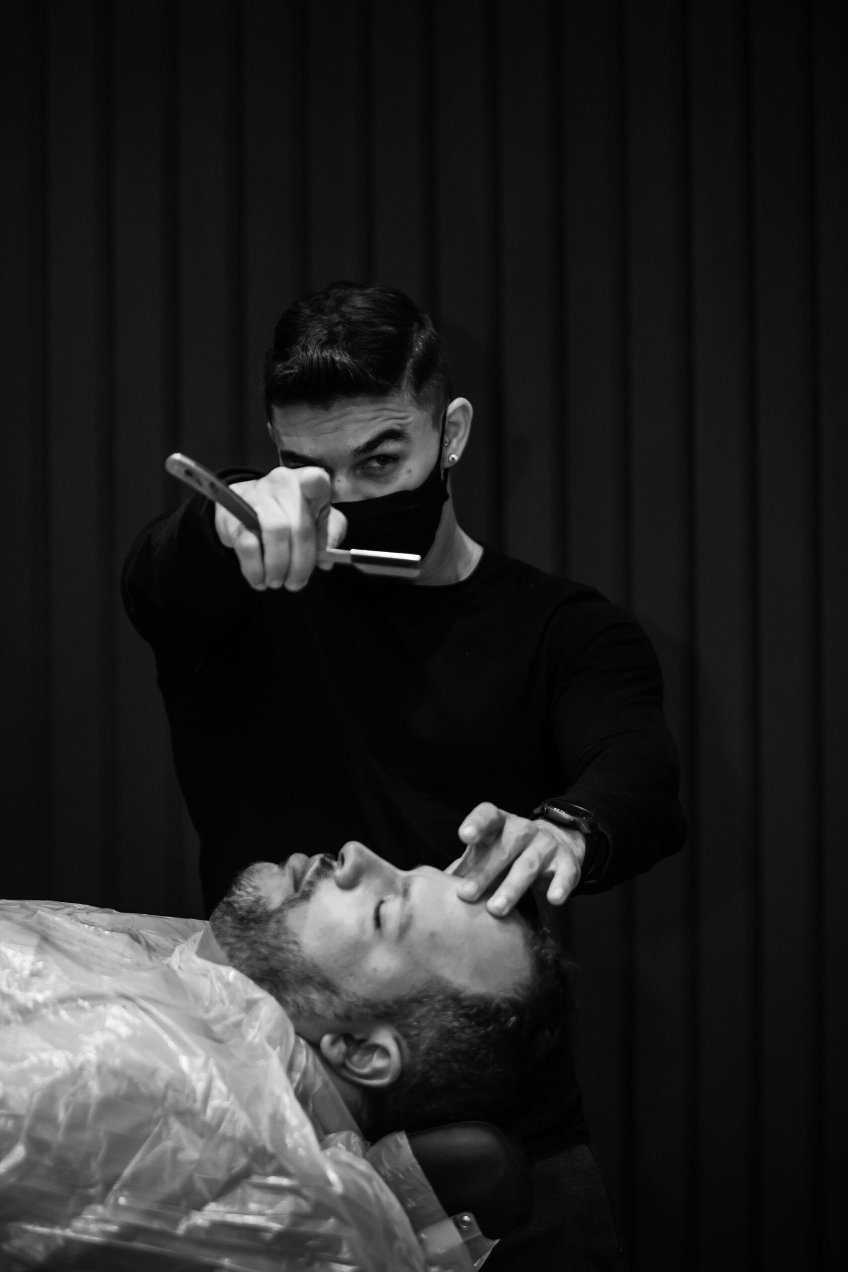 Barber holding a straight razor over a reclined client, black and white
