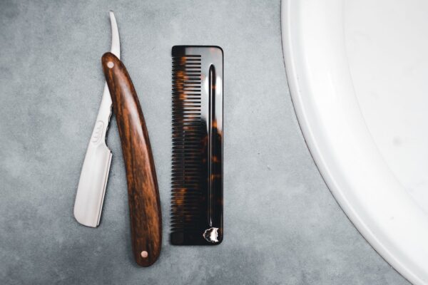 Wood handled straight razor next to a tortoiseshell pocket comb