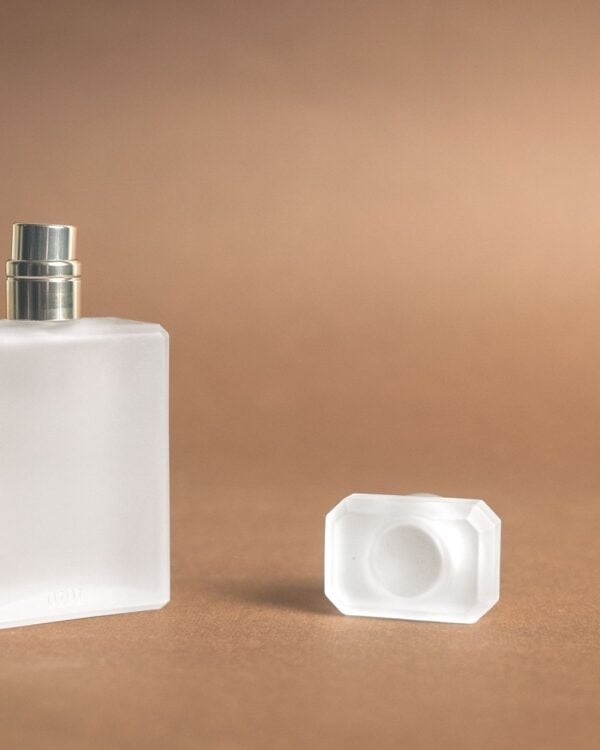 Frosted glass perfume bottle on a warm beige background