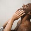 Close-up portrait of a man touching his face in a tiled bathroom