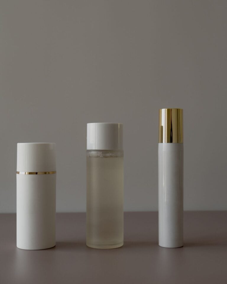 Three white bottles with gold caps on a grey surface