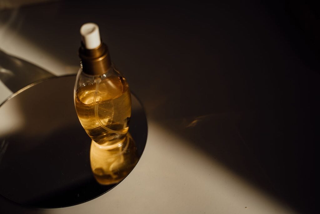 Golden body oil bottle on a mirror in a beam of warm light