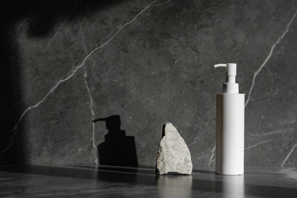 White pump bottle and a raw stone against dark marble
