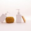 White pump bottle, sponge and wooden brush on a pale surface