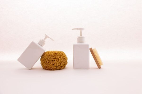 White pump bottle, sponge and wooden brush on a pale surface