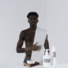 Man with a towel over his shoulder beside skincare bottles