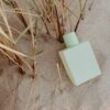 Pale green perfume bottle resting in beach grass and sand