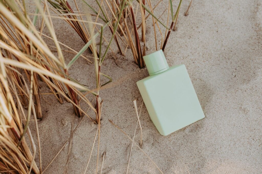 Pale green perfume bottle resting in beach grass and sand