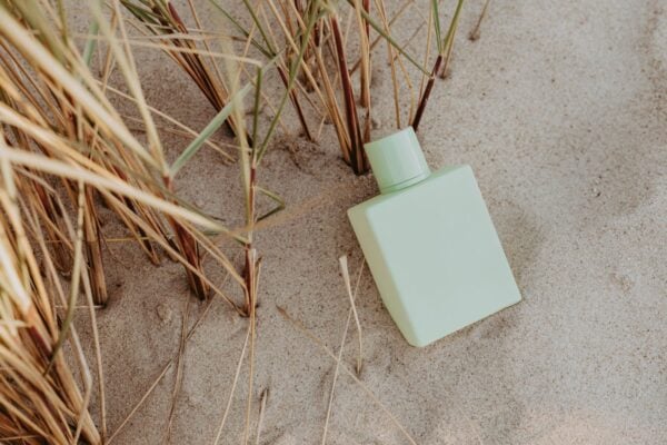 Pale green perfume bottle resting in beach grass and sand