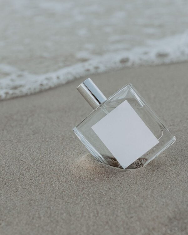 Clear perfume bottle standing on wet sand by the sea